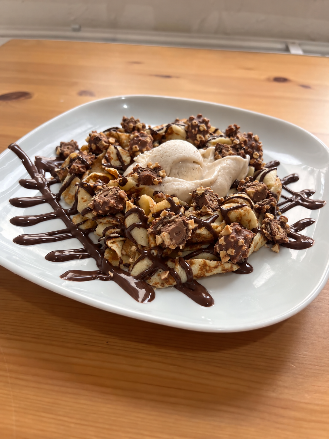 Crêpe en tagliatelles Ferrero, morceaux de Ferrero Rocher, coulis chocolat, une boule de glace vanille et chantilly. Suggestion de présentation ; accompagnements servis à part.
