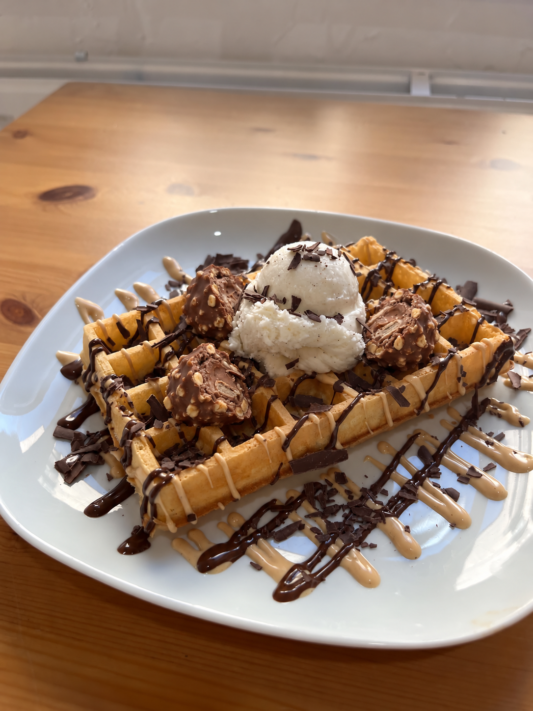 Gaufre de Bruxelles Ferrero avec morceaux de Ferrero Rocher, coulis Ferrero, une boule de glace vanille et chantilly. Suggestion de présentation ; accompagnements servis à part.